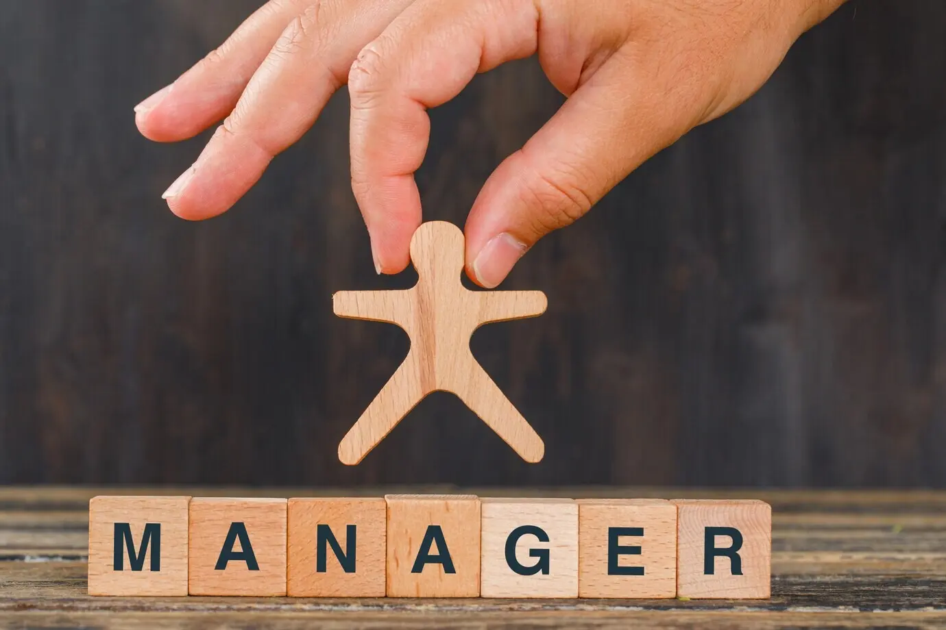 Концепция управления с деревянными кубиками на деревянном столе, вид сбоку; рука держит модель человека.